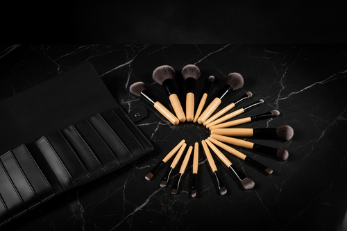 24-piece professional makeup brush set fanned out on black marble with leather roll case